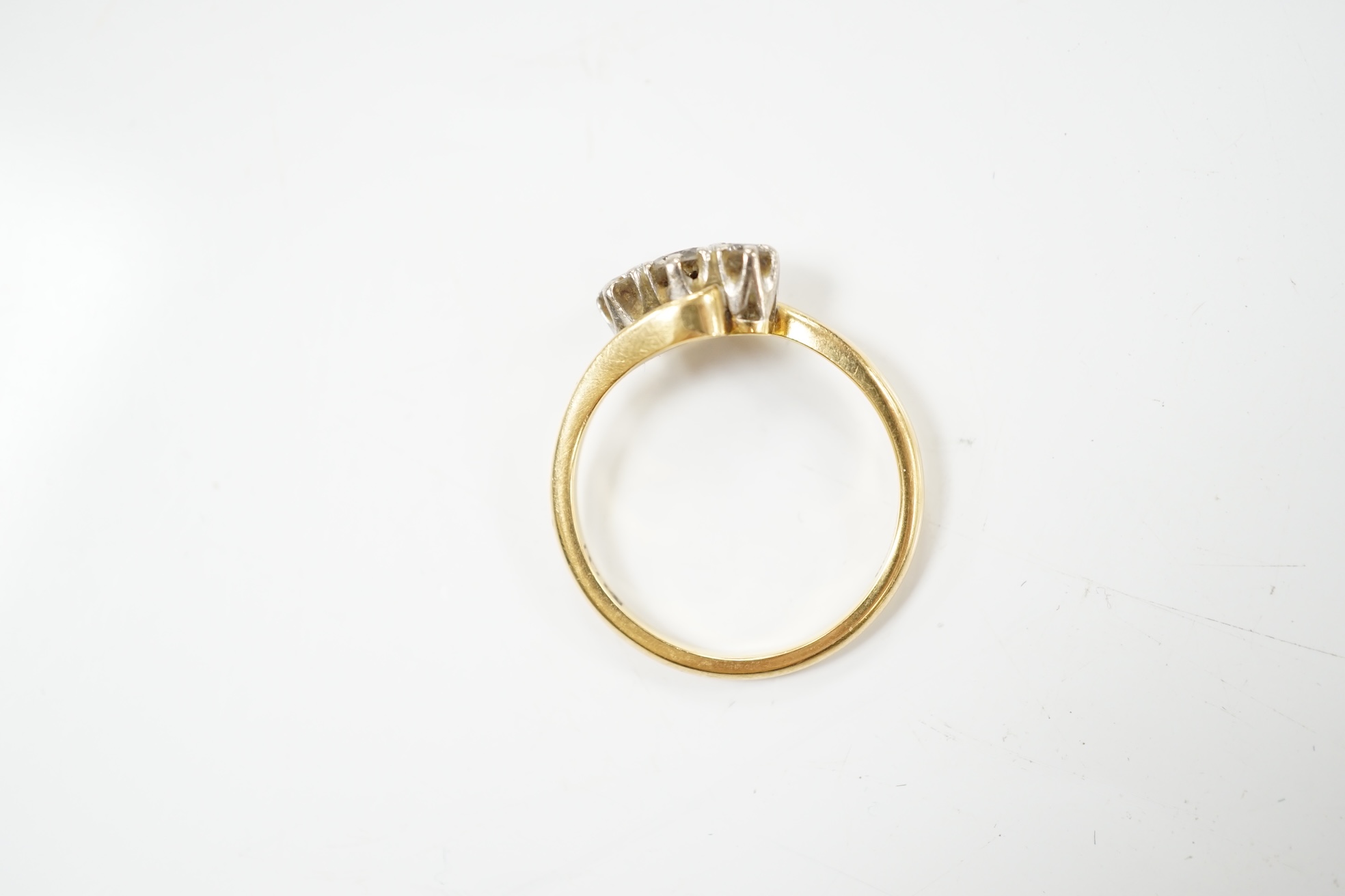 A modern `18ct gold and three stone diamond set crossover ring, size O, gross weight 3.4 grams. Condition - fair